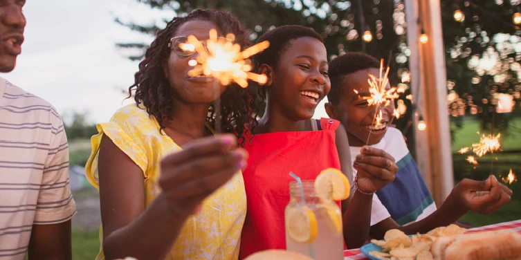 African American family sitting at picnic table with sparklers.