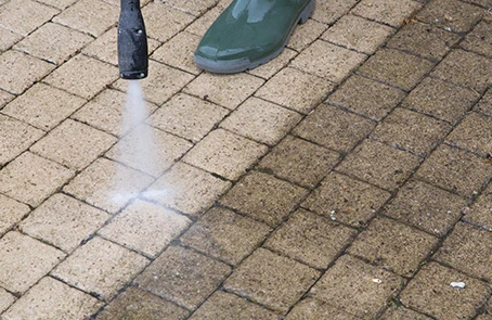 A service professional pressure washing a stone walkway.