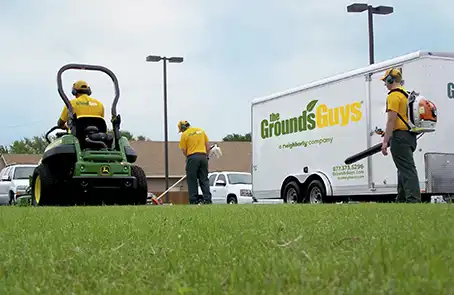 Three Grounds Guys employees performing lawn cleanup next to company trailer.