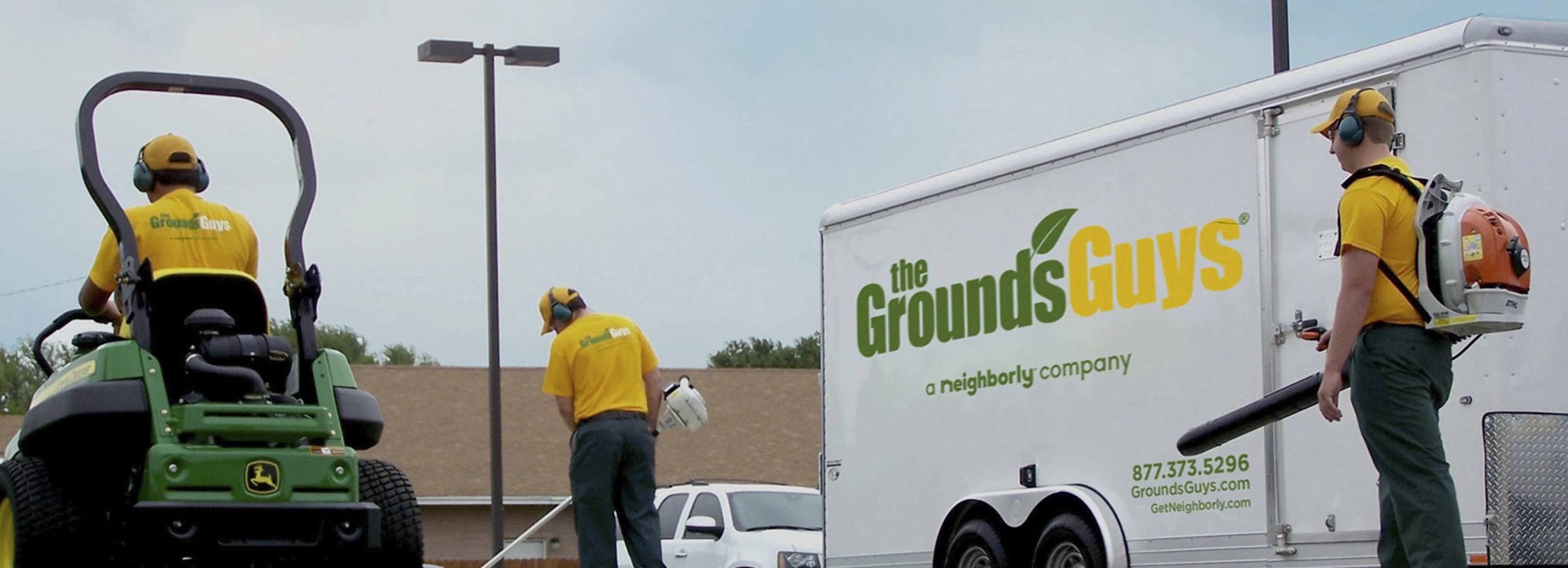 Three Grounds Guys employees performing lawn cleanup next to company trailer.