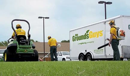 Three Grounds Guys service professionals performing lawn cleanup next to a branded company trailer.