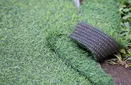 A piece of artificial turf grass installed on the ground, with a corner pulled up.